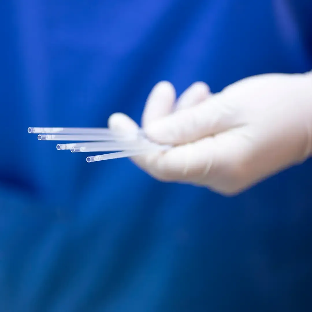 A gloved hand holds several thin, clear medical semen straws against a blurred blue background.