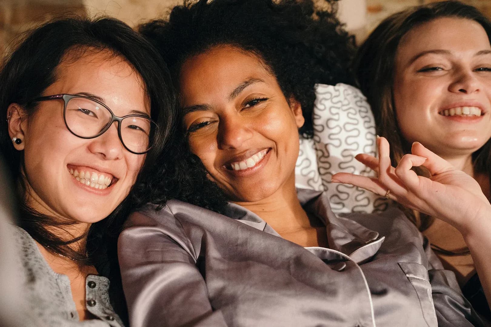 group of three female friends sharing a sofa together smiling for the camera