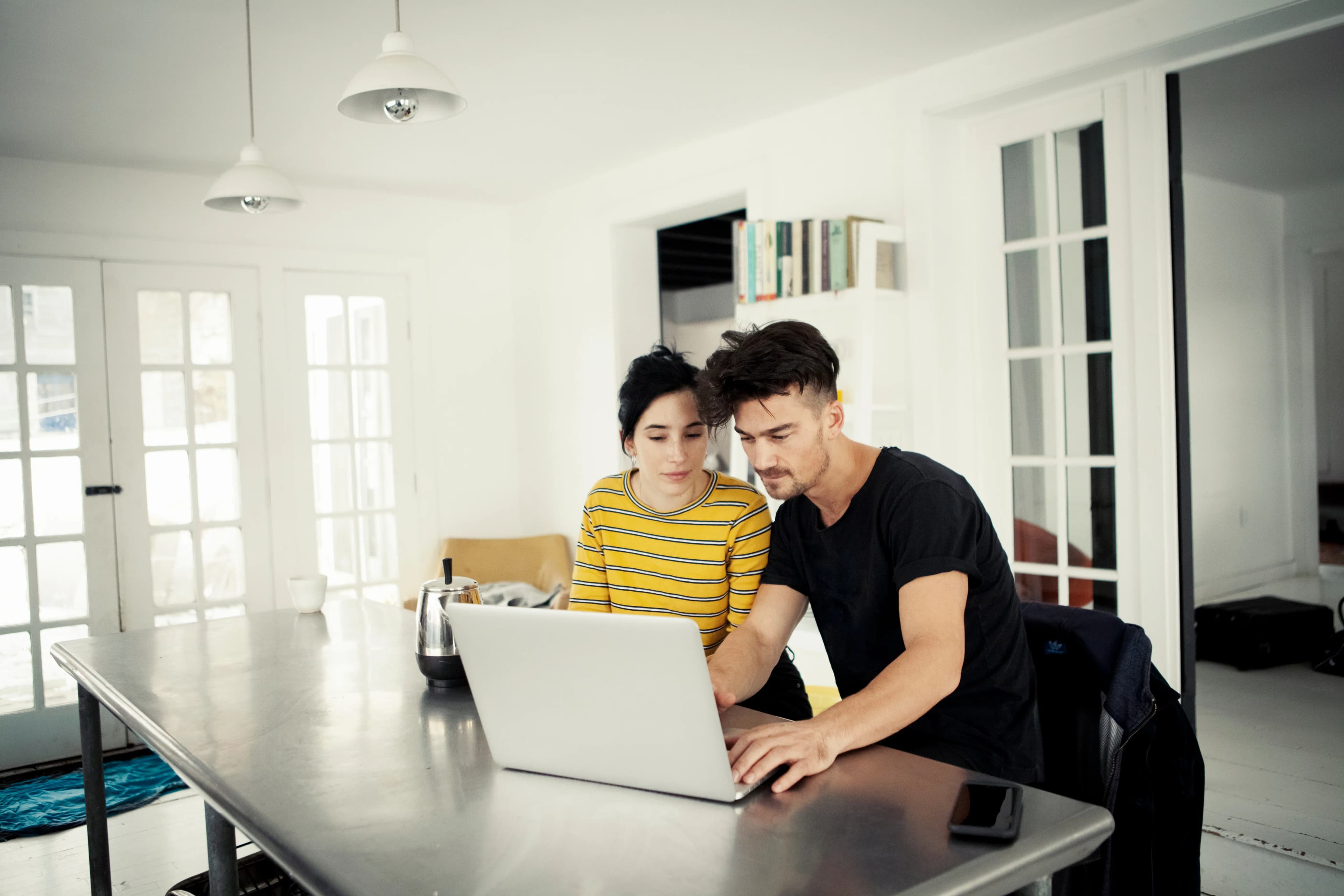 A young couple sat at a dining table looking at a laptop